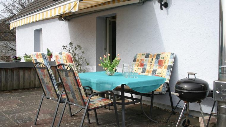 Een gezellige buitenruimte met een tafel en vier stoelen. Op de tafel staat een vaas met bloemen en een barbecue is in de buurt.