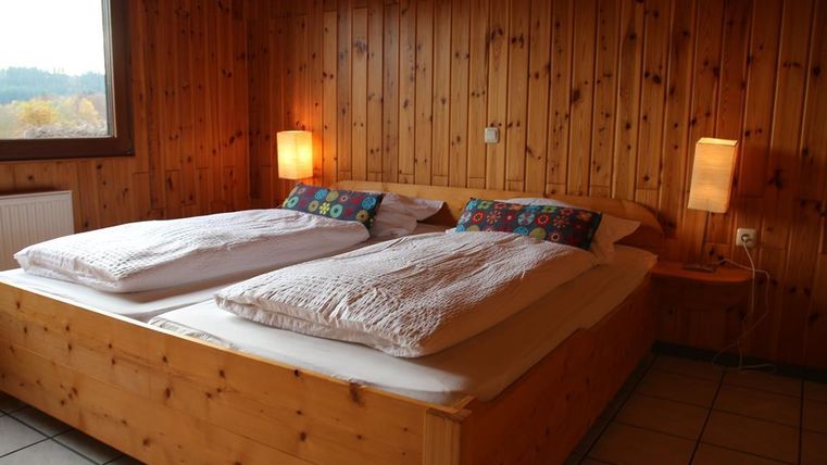Ein gemütliches Schlafzimmer mit einem Holzbett und bunten Kissen. Die Wände sind mit Holzpanelen verkleidet und es gibt zwei Lampen für sanftes Licht.