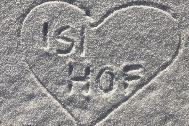 Een hartvorm in de sneeuw met de opdruk "ISI HOF". De letters zijn duidelijk zichtbaar en steken af tegen de witte ondergrond.