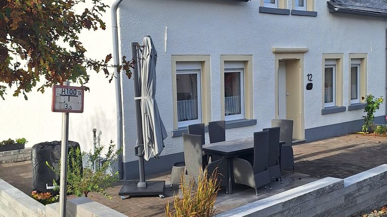 Ein gepflegtes Haus mit hellem Anstrich und einem kleinen Vorgarten. Die Straße ist ruhig mit einem klaren blauen Himmel im Hintergrund.