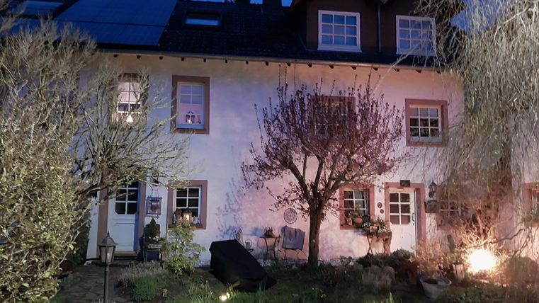 Een charmant huis met een bloeiende boom in de tuin. De avonddlucht en de zachte verlichting creëren een gezellige sfeer.