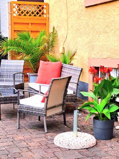 Ein gemütlicher Außenbereich mit Rattanmöbeln und bunten Pflanzen. Die Sitzecke lädt zum Entspannen ein.