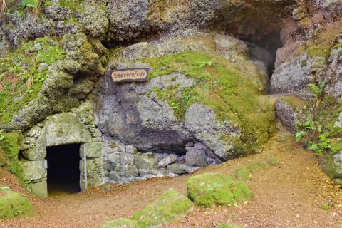 Höhleneingang in moosbedecktem Felsen, Schild 'Schwedenfeste'. Naturpfad führt zur Öffnung. Mystische Atmosphäre.