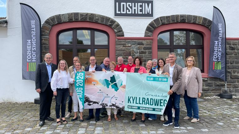 Vertreter der Ortsgemeinden entlang der Strecke und Politiker stehen dicht beeinander und halten das Veranstaltungsbanner hoch.