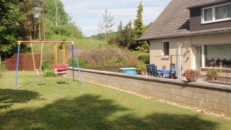 Ein gepflegter Garten mit einer Schaukel und Sitzgelegenheiten. Im Hintergrund steht ein modernes Haus, umgeben von Bäumen.