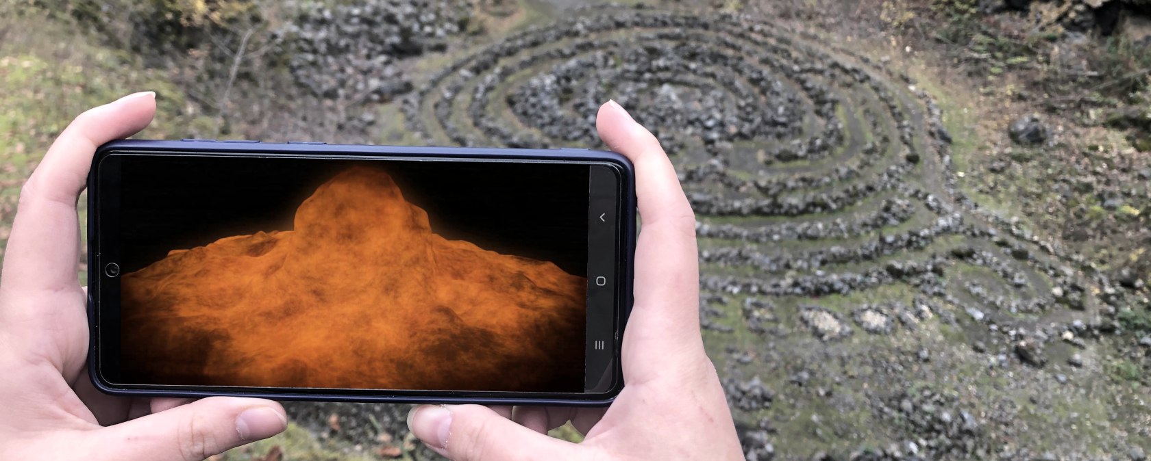 Twee handen houden een smartphone over de afgrond van een vulkaan. De vulkaanexplosie wordt op het scherm gevisualiseerd.