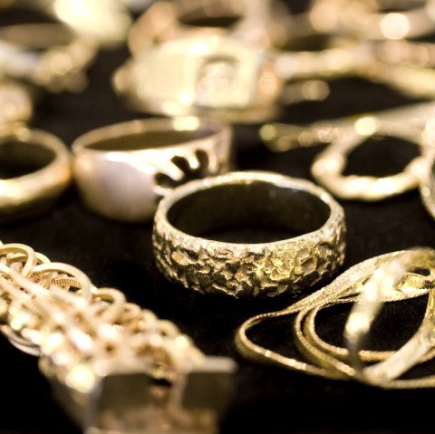 Nahaufname mehrerer goldener Ringe, Armb&auml;nder und Ketten auf schwarzem Grund.