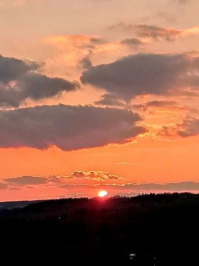 Ein wunderschöner Sonnenuntergang über den Hügeln mit leuchtenden orange- und Rottönen. Wolken ziehen langsam am Himmel vorbei.
