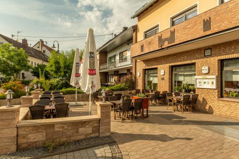Terrasse des Restaurants mit Tischen, Stühlen und Sonnenschirmen. Die Umgebung ist grün und das Wetter sonnig.