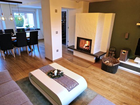 Ein gemütliches Wohnzimmer mit einem modernen Kamin und einer hellen, einladenden Atmosphäre. Der Tisch ist festlich dekoriert und es gibt einen Blick auf den Essbereich.