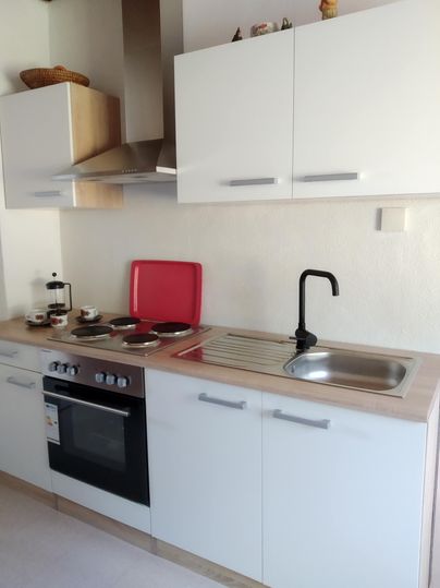 Une cuisine moderne avec des placards blancs et un plan de travail en bois clair. Les zones de préparation sont propres et bien organisées.