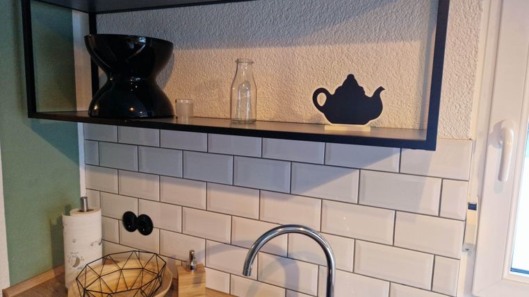 Eine moderne Küche mit einer schwarzen Regale und stilvollen Dekorationsobjekten. Die weißen Fliesen und Holzoberflächen schaffen eine warme Atmosphäre.