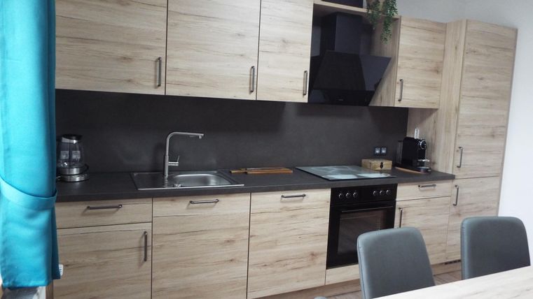 Eine moderne Küche mit Holzschränken und einem dunklen Arbeitsbereich. Sie ist gut ausgestattet mit Herd, Spüle und Küchenutensilien.