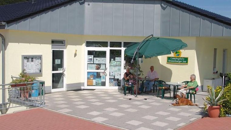 Blick auf den Eingangsbereich des Bistro.Ein gelbgestrichenes Gebäude mit zwei Eingangstüren. Vor dem Haus ist eine gepflasterte Terrasse mit mehreren Tischen und Stühlen.