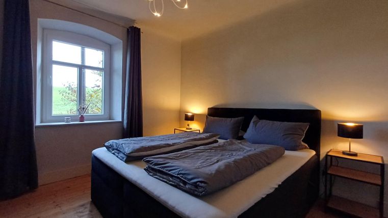 Een gezellige slaapkamer met een groot bed en moderne nachtkastjes. Het raam biedt daglicht en de gordijnen zijn donker en elegant.