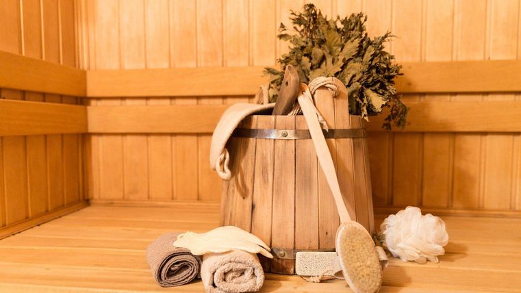 Ein Holzeimer mit Saunazubehör, Handtüchern und einem Aufgussbesen in einer Sauna aus Holz.