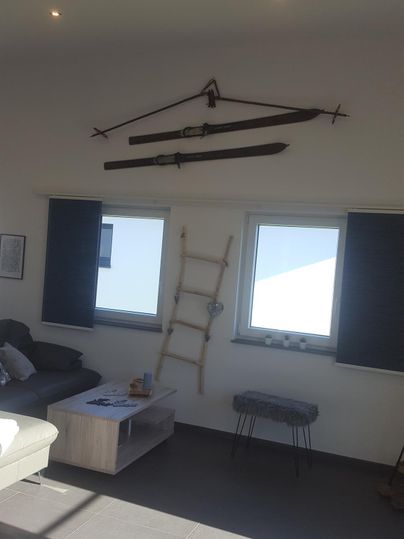 Ein modernes Wohnzimmer mit einem Sofa und einem Tisch. An der Wand hängen dekorative Schwert- und Bauernutzen-Zubehör, neben Fenstern und einer Holzleiter.