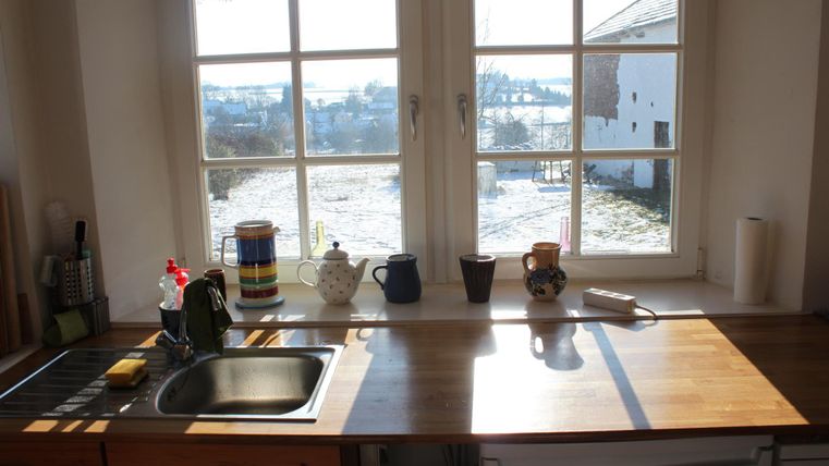 Een lichte keuken met een houten werkblad en uitzicht uit het raam op een winterse landschap. Op het aanrecht staan enkele keukengerei en decoratieartikelen.