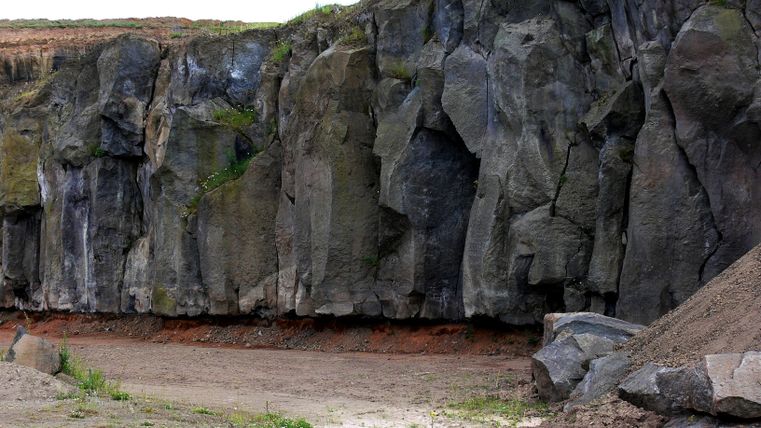 Steinbruch mit hohen Felswänden und Vegetation.
