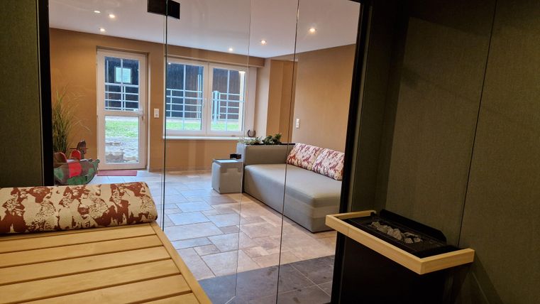 Ein modernes Entspannungsraum mit einer Sauna und einer bequemen Couch. Große Fenster bieten einen Blick ins Freie.