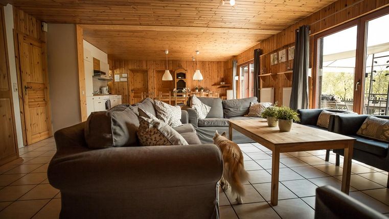 Ein gemütliches Wohnzimmer mit Holzwänden und modernen Möbeln. Ein runder Tisch steht in der Mitte, umgeben von bequemen Sofas und einem Fensterblick nach draußen.