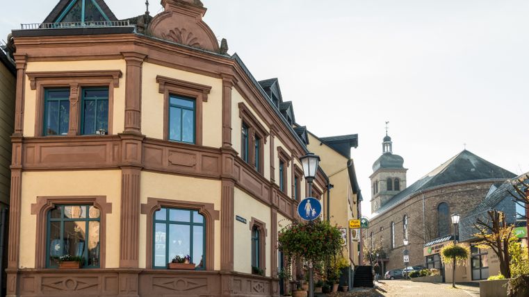 Straßenszene in Hillesheim mit historischem Gebäude und Kirche im Hintergrund.