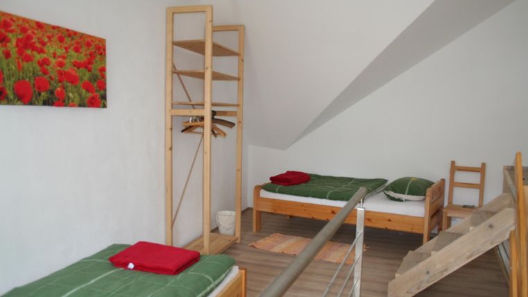 Een lichte kamer met twee eenpersoonsbedden en een minimalistische inrichting. Aan de muur hangt een schilderij met rode bloemen.