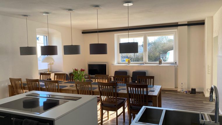 Eine moderne Küche mit einem großen Esstisch und Holzstühlen. Helle Wände und große Fenster sorgen für viel Licht im Raum.