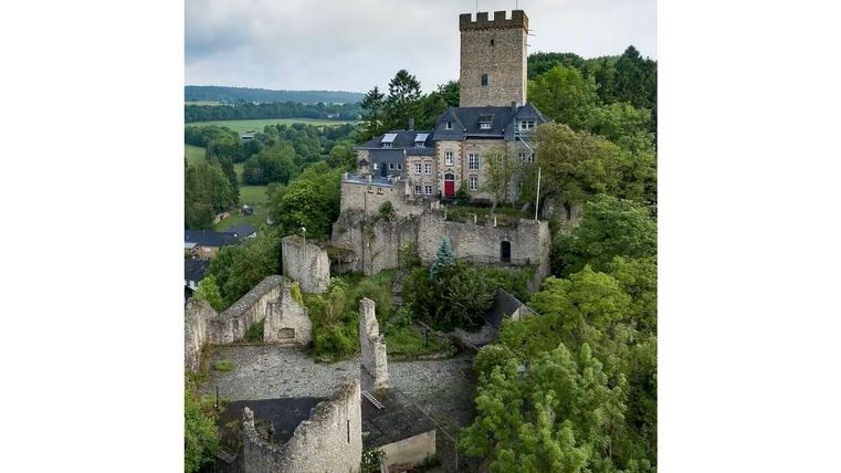Eine beeindruckende Burg auf einem Hügel, umgeben von grünen Bäumen. Der Turm ragt über die Ruinen der alten Strukturen hinaus.
