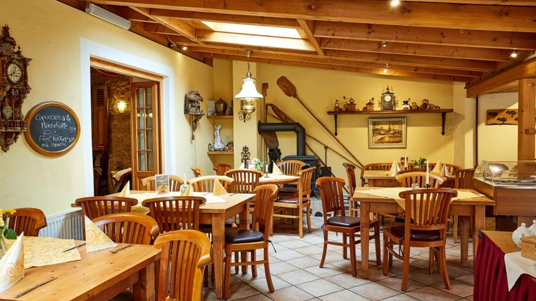 Ein gemütliches Café mit Holzmöbeln, rustikaler Dekoration und einer Tafel mit Getränkepreisen. Die Decke ist aus Holz, der Boden gefliest.