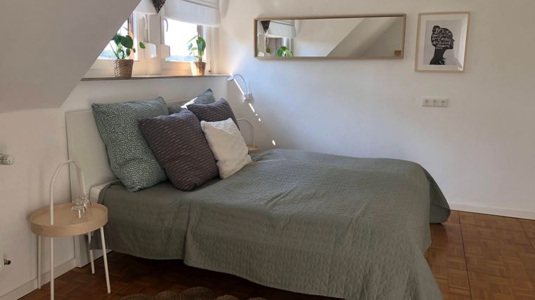 Ein gemütliches Schlafzimmer mit einem Doppelbett und mehreren Kissen. Ein kleiner Tisch steht daneben, und die Wände sind hell und modern dekoriert.