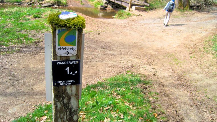 Wandelpad met wegwijzer en brug op de achtergrond.
