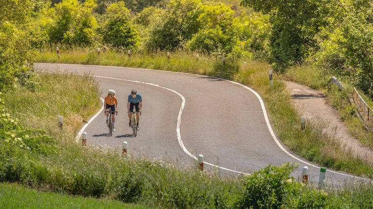 Zwei Radfahrer auf einer kurvigen Landstraße in der Eifel.