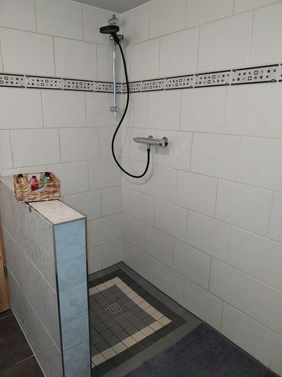 Een moderne douche met witte tegels en elegante accenten. Op de plank staan enkele verzorgingsproducten in een decoratieve mand.