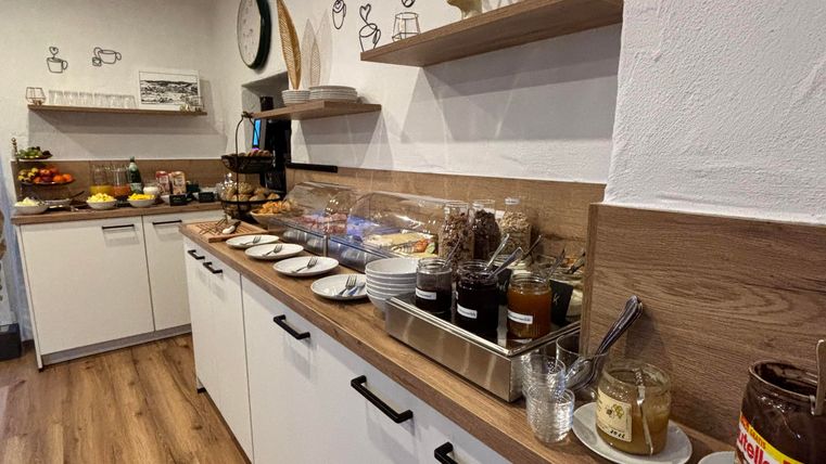 Eine moderne Küche mit Holzregalen und einer langen Arbeitsfläche. Auf der Theke stehen verschiedene Lebensmittel und Getränke bereit.