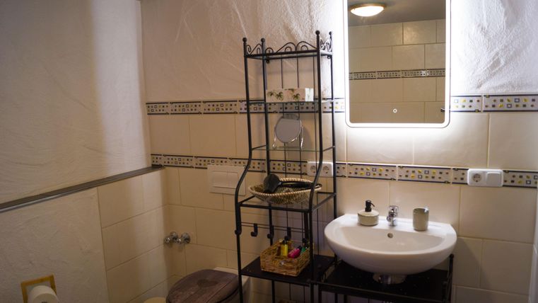 Een badkamer met een moderne wastafel en een spiegel. Een plank met verschillende benodigdheden en een toilet is ook zichtbaar.