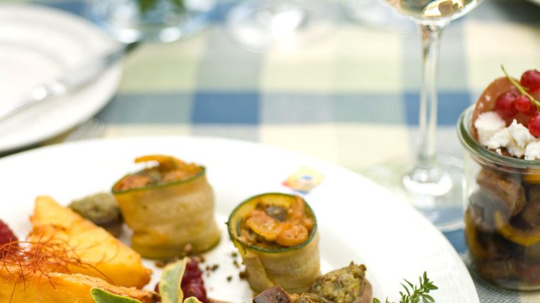 Une assiette artistiquement dressée avec des rouleaux de courgettes farcis, des baies et une portion de potiron. Accompagnée d'un verre de vin blanc et d'un petit verre de légumes marinés.