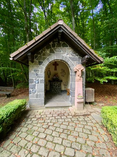 Die kleine Arnulphuskapelle mit Altar und bemalten Wänden im Innenraum vor einem Laubwald.