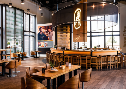 Restaurantraum der Bitburger Brauerei mit vielen Tischen, Stühlen und einer runden Theke in der Mitte. Große Fensterwände und passender Dekoration.