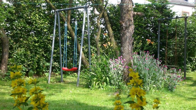 Ein schöner Garten mit Schaukeln und bunten Blumen. Die grüne Rasenfläche lädt zum Spielen ein.