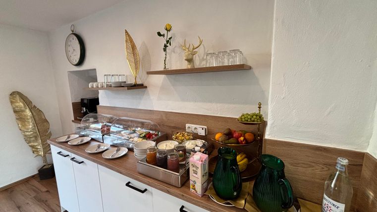 Eine moderne Küche mit einem Holzregal und einer Auswahl an Snacks. Auf der Theke stehen Geschirr, Früchte und Getränke bereit.