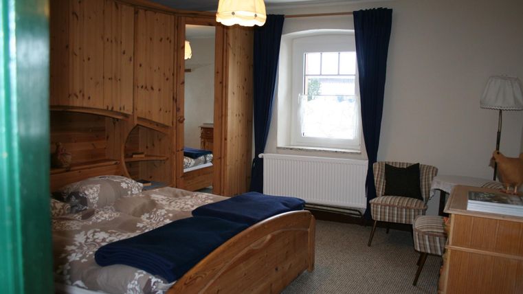 Een gezellige slaapkamer met houten details en een groot bed. Er is een stoel en een raam met gordijnen.