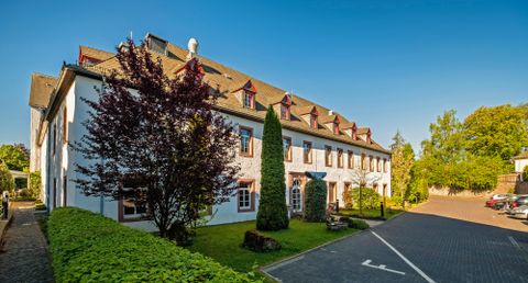 Un bâtiment moderne avec des murs blancs et des fenêtres rouges. Le jardin est vert avec des arbres et des buissons.