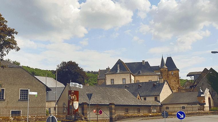 Historische Burganlage Lissingen mit Türmen und Gebäuden, umgeben von Bäumen. Ein Kreisverkehr und ein Schild im Vordergrund.