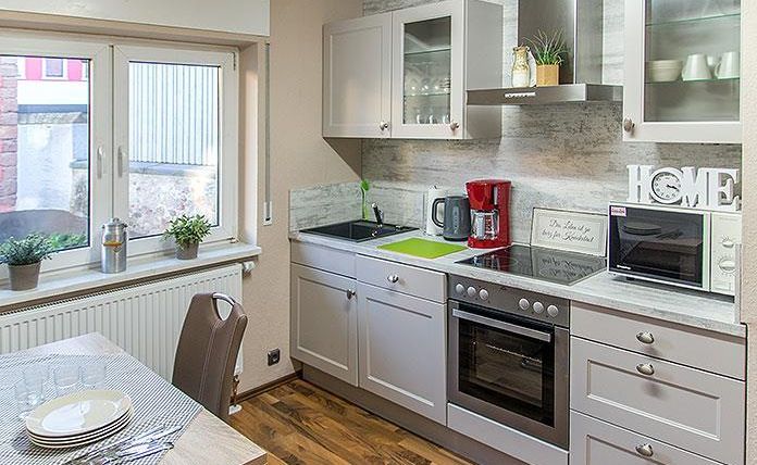 Een moderne keuken met lichte kasten en elegante apparaten. De tafel is gedekt en een raam zorgt voor natuurlijk licht.