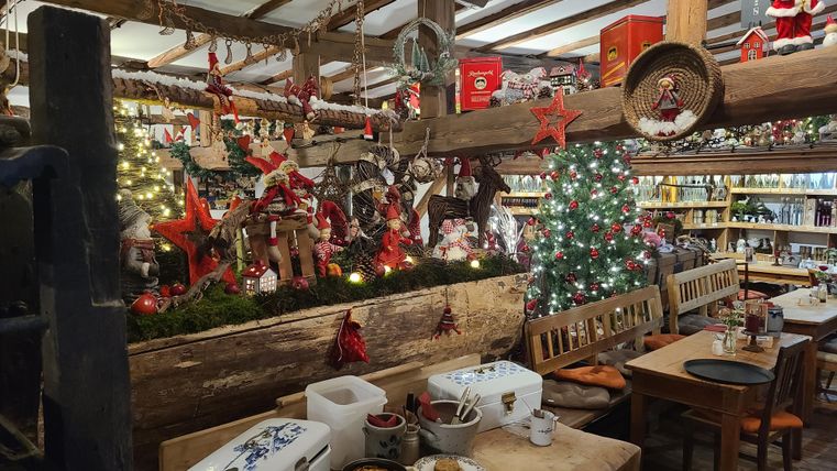 Ein gemütlich dekorierter Raum für die Weihnachtszeit mit einem Weihnachtsbaum und festlicher Dekoration. Auf den Tischen stehen verschiedene Leckereien und das Ambiente ist einladend.