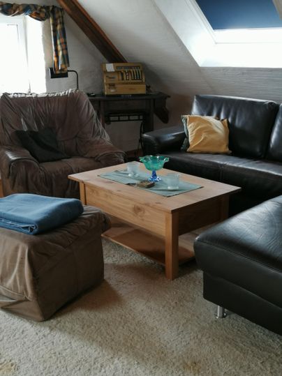 Een gezellige woonkamer met een houten salontafel en twee comfortabele stoelen. Op de tafel staat een glazen vaas en een paar kussens op de bank.