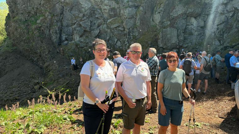 Zahlreiche Wanderer vor einer massiven Steinwand. Im Vordergrund 3 Wanderer nebeneinander.