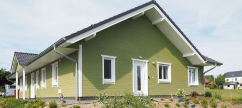 Ein modernes, grün gestrichenes Haus mit einem Satteldach. Es hat große Fenster und liegt in einer ruhigen Umgebung.