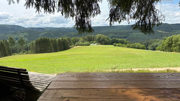 View from a table and a bench onto a green meadow with a forest in the background.